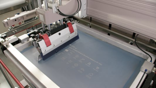 Video still of a printer head moving across a clear sheet, leaving the product name and characteristics printed as a demo