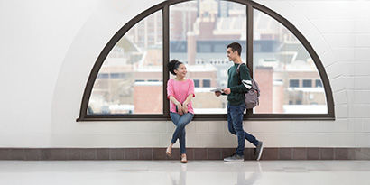 Two young people chatting in front of a large window and clean, shiny floors.